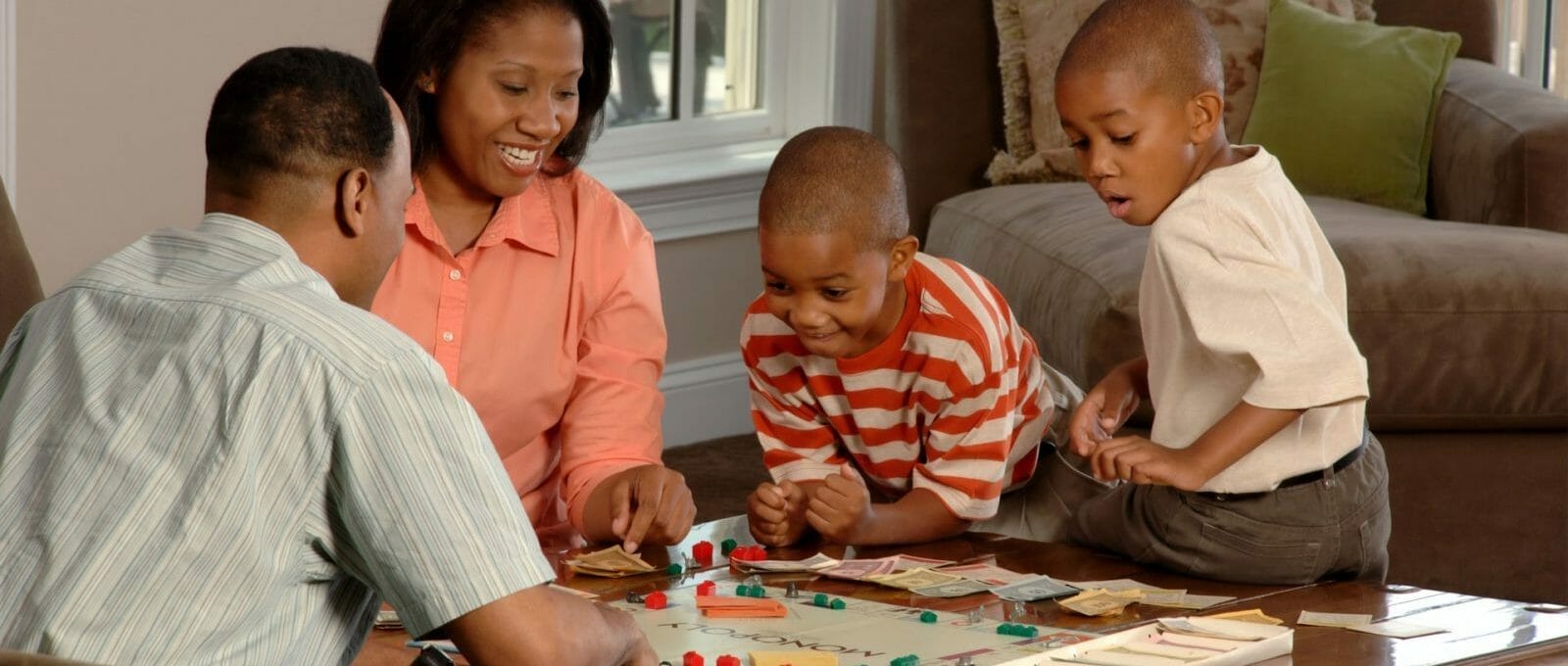 Pai, mãe e dois filhos sorrindo enquanto brincam com jogo de tabuleiro na mesa da sala