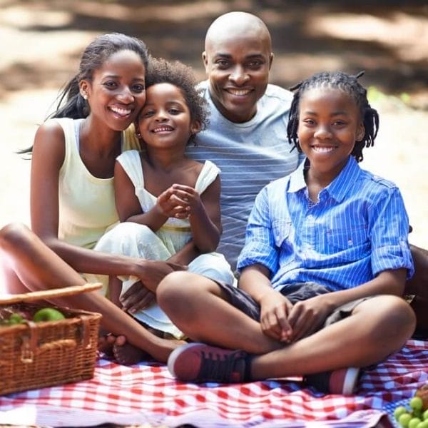 família sentada em cima de toalha de mesa para fazer piquenique com as crianças