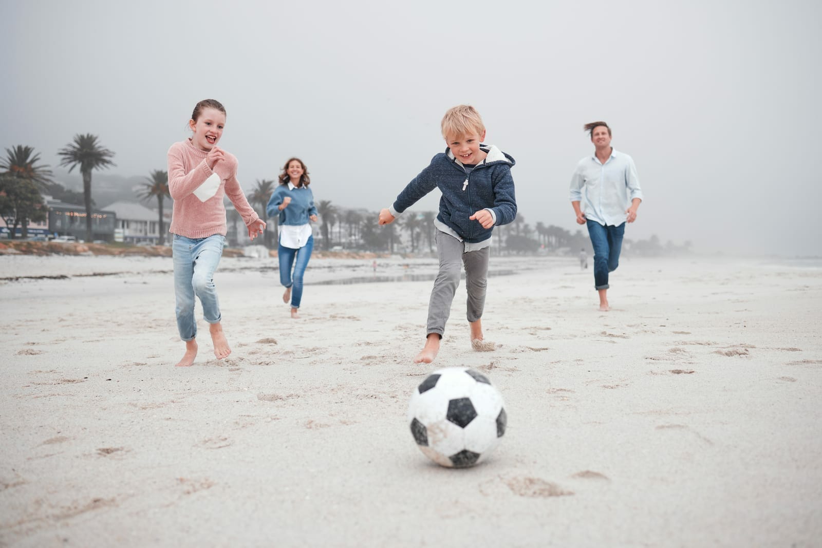 Família com pai, mãe e duas crianças jogando futebol na praia