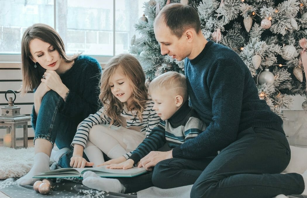 Pais e duas crianças pequenas sentados no chão e lendo juntos