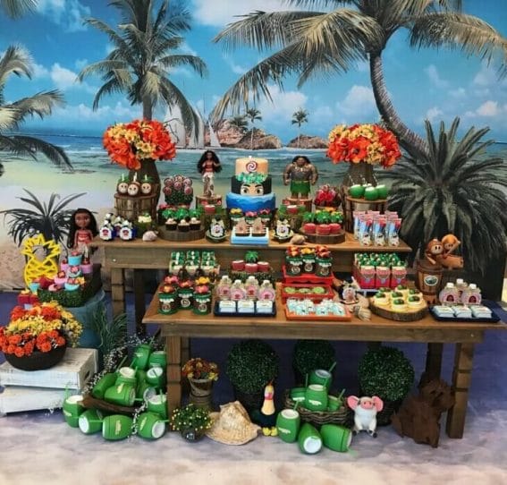 mesa de doces de festa infantil moana, com painel com imagem de praia no fundo
