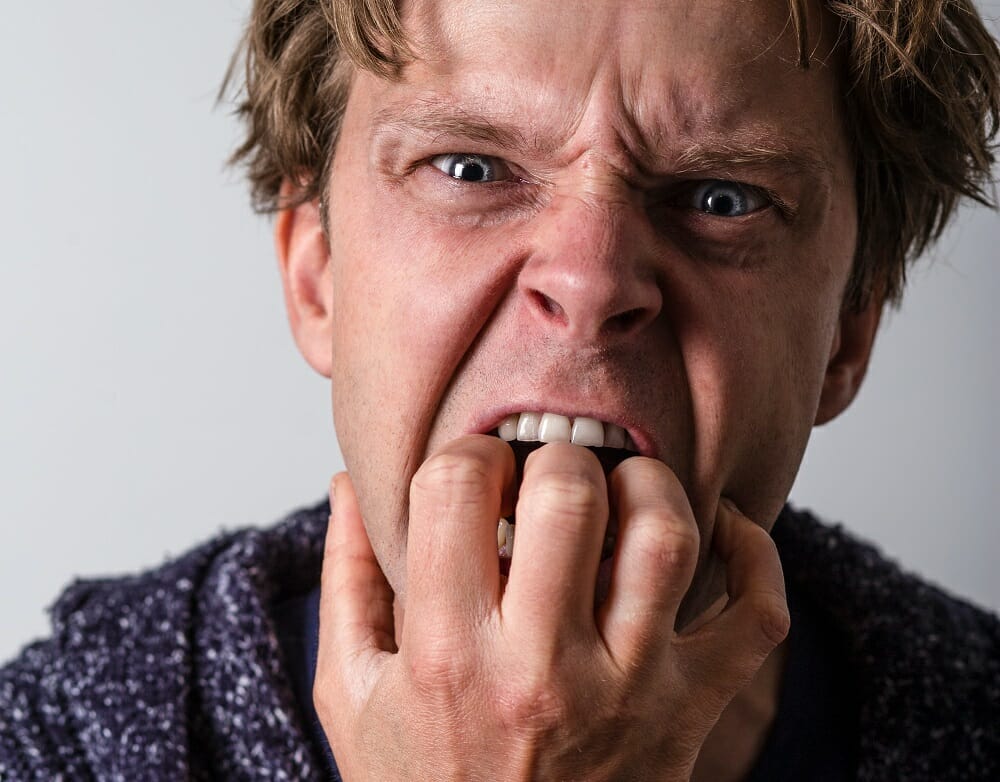 homem nervoso com a mão na boca roendo unhas