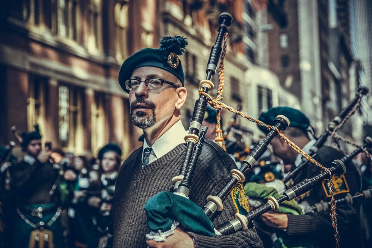 Imagens de um desfile irlandês. país de origem do nome Gael. Em destaque, um homem vestido com trajes típicos e segurando uma gaita de fole.