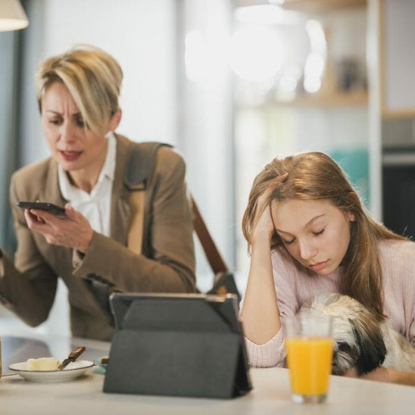 mãe de roupa social está gritando com o telefone. a filha adolescente está sentada ao lado, com cara emburrada por causa da briga