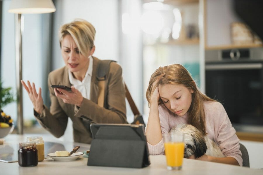 mãe de roupa social está gritando com o telefone. a filha adolescente está sentada ao lado, com cara emburrada por causa da briga