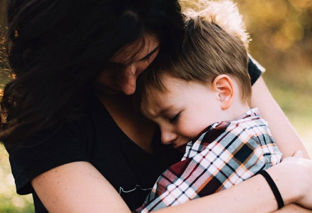 Filho chorando no colo da mãe, que abraça a criança para consolar