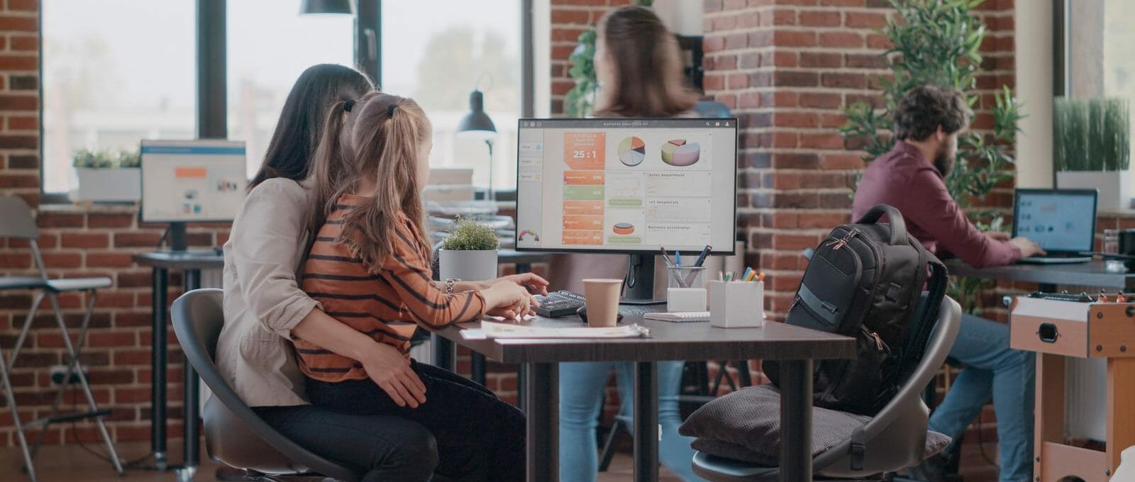 Mãe trabalhando em um computador no escritório com uma criança no colo