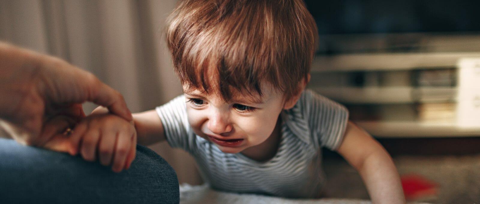 Criança chorando no chão depois de cair, tentando se levantar. Ele apoia um dos braços na mãe