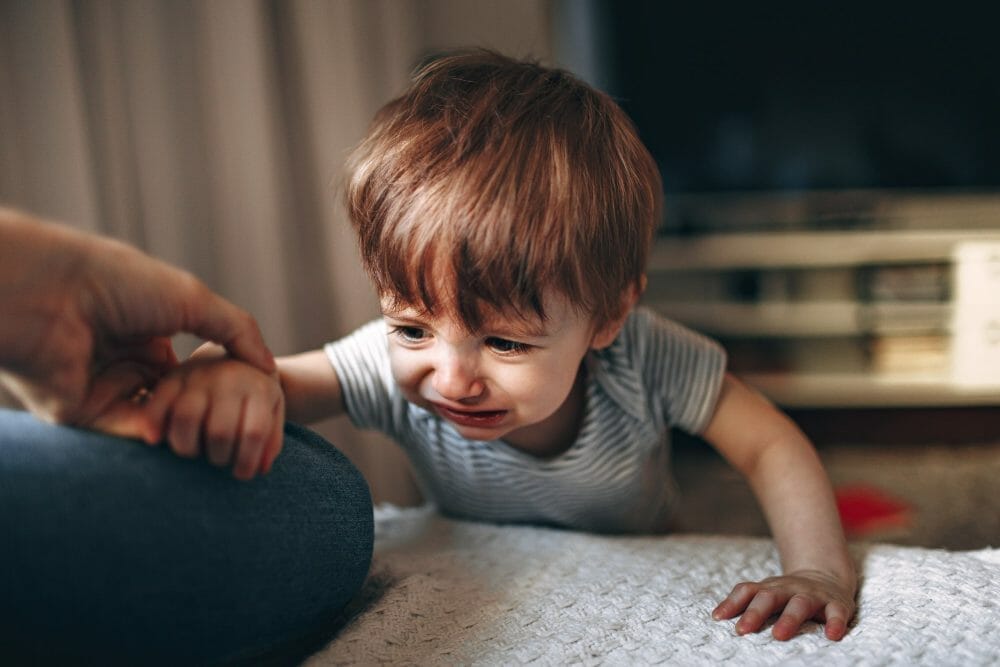 Criança chorando no chão depois de cair, tentando se levantar. Ele apoia um dos braços na mãe