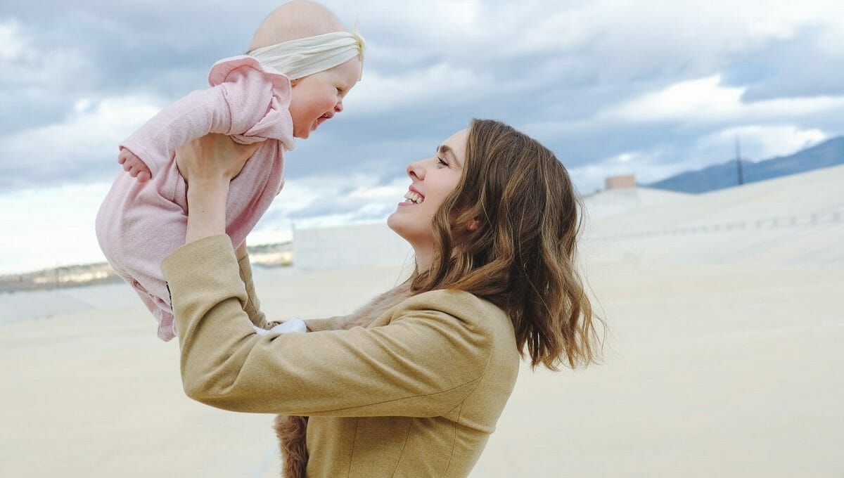 Mãe segurando bebê de seis meses no ar; ambas sorriem