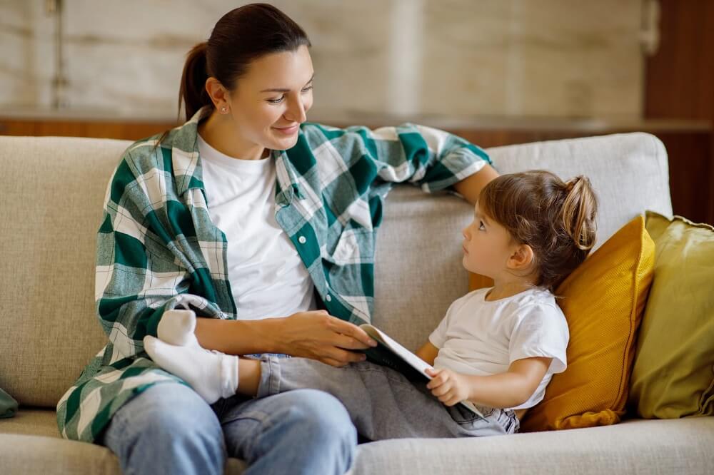 mãe no sofá lendo com a filha, simbolizando o conceito de criar filho sozinha