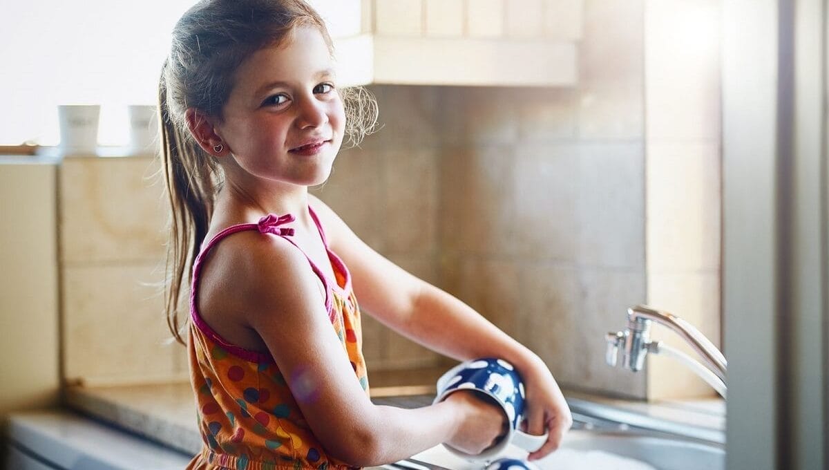 menina lavando louça para ajudar em casa com tarefas domésticas