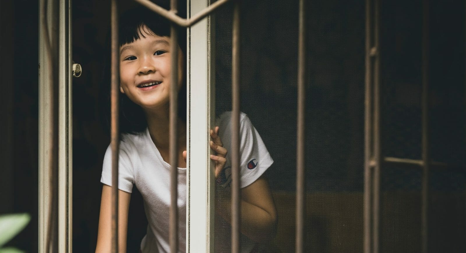 menina oriental olhando pela janela, por de trás de grades.