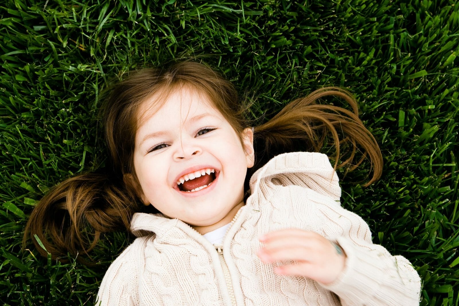 menina deitada na grama e sorrindo para a câmera