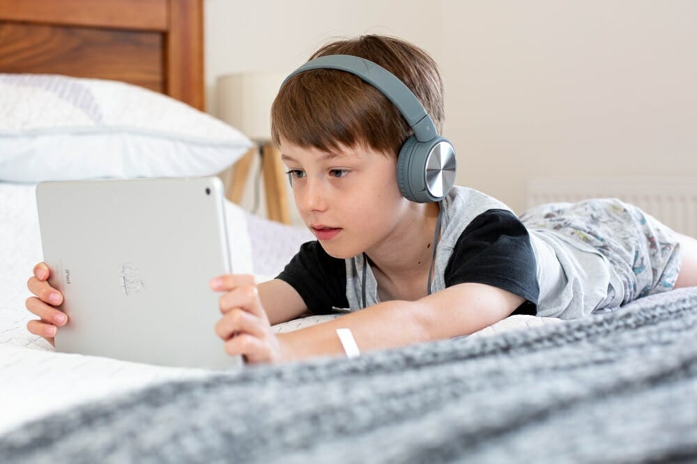 Menino deitado na cama usando tablet