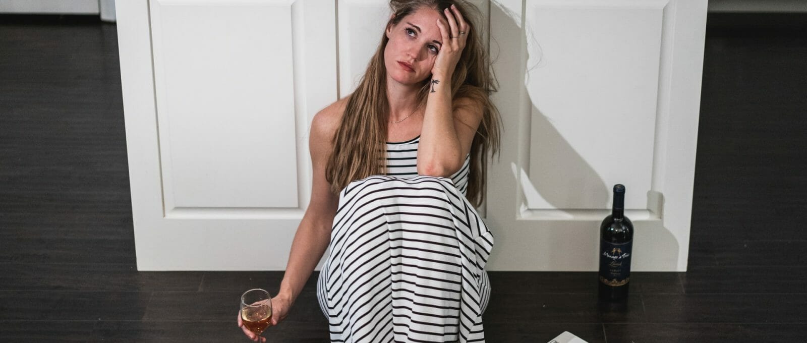 Mulher desolada sentada no chão da cozinha, bebendo vinho