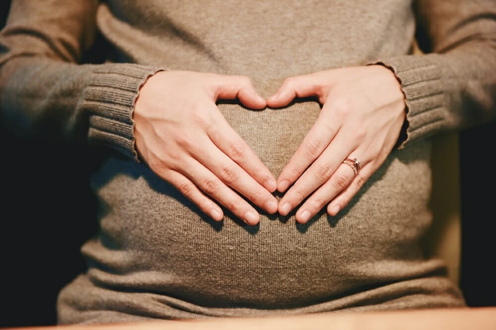 mulher grávida fazendo coração com as mãos sobre a barriga
