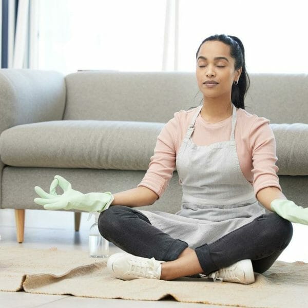 mulher meditando sentada no chão da sala, com um balde de limpeza ao seulado