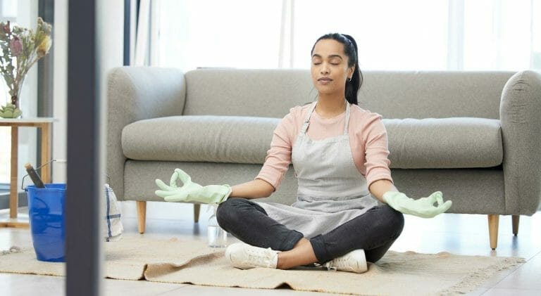 mulher meditando sentada no chão da sala, com um balde de limpeza ao seulado