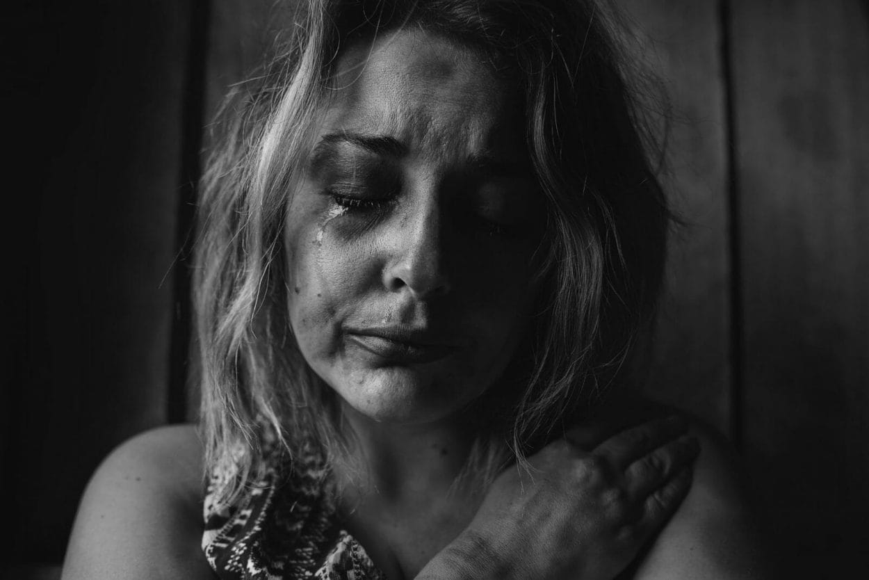 retrato em preto e branco de uma mulher com o rosto abatido e chorando