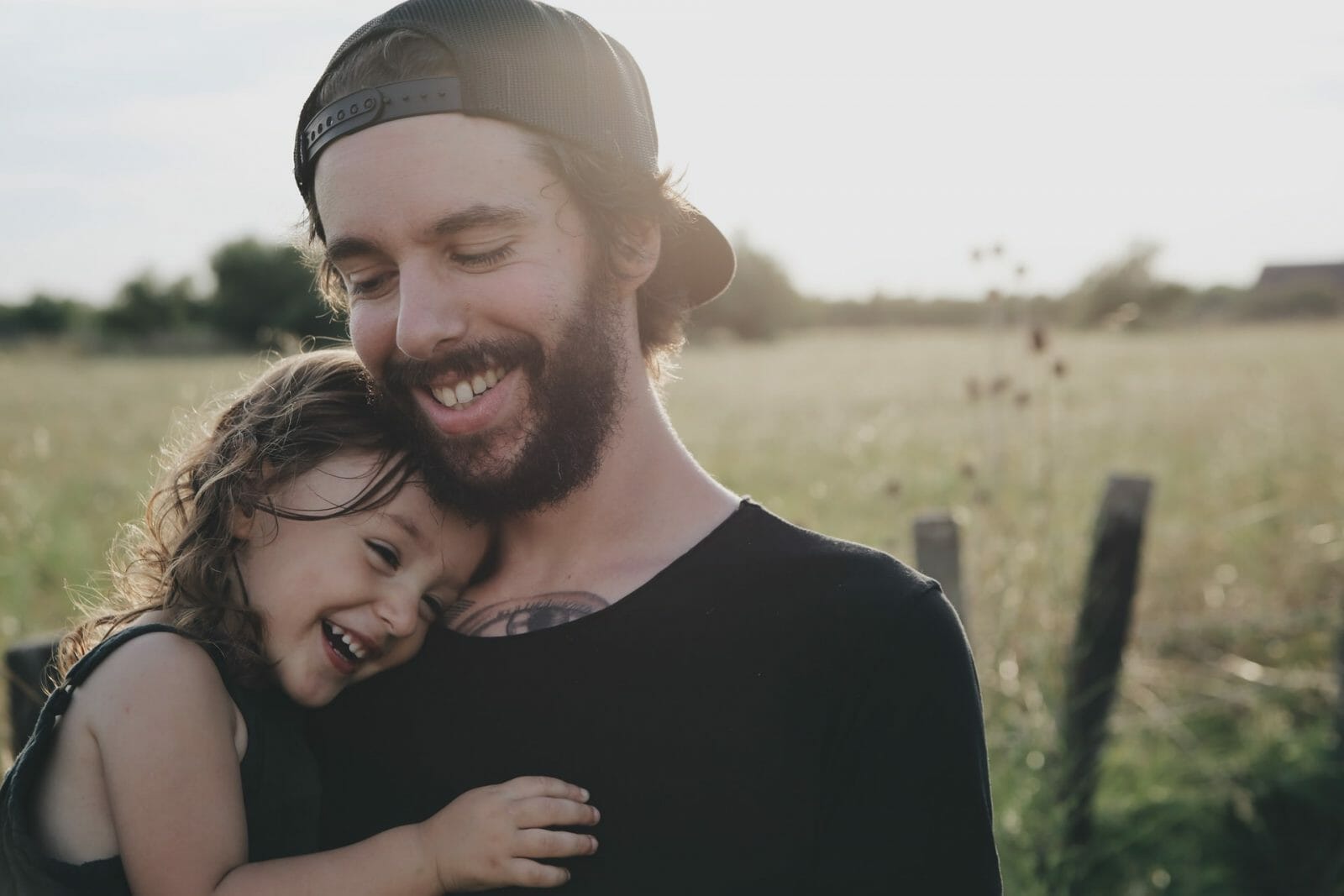 filha sorrindo no colo do pai em um espaço aberto