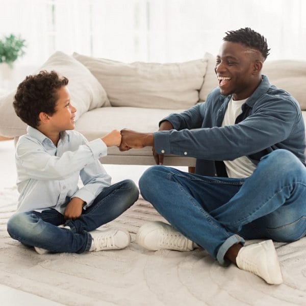 pai e filho sentados na sala dando um soquinho, representando o conceito de parceria e de ser amigo do seu filho