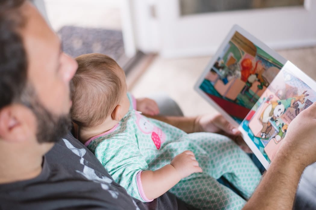 Pai com filho bebê sentado no colo lendo um livro infantil