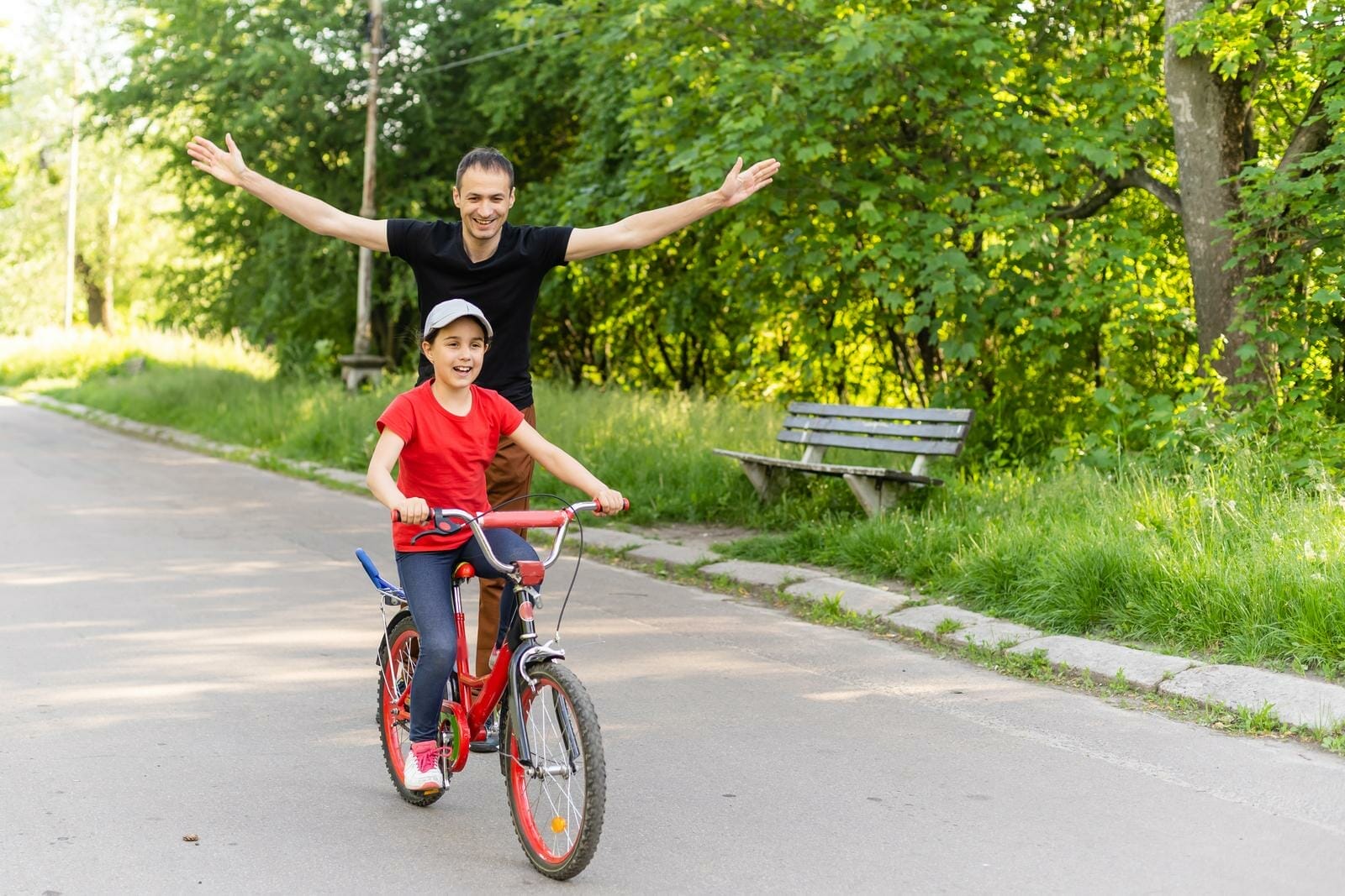Pai orgulhoso da filha andando de bicicleta sozinha, acompanhando de perto