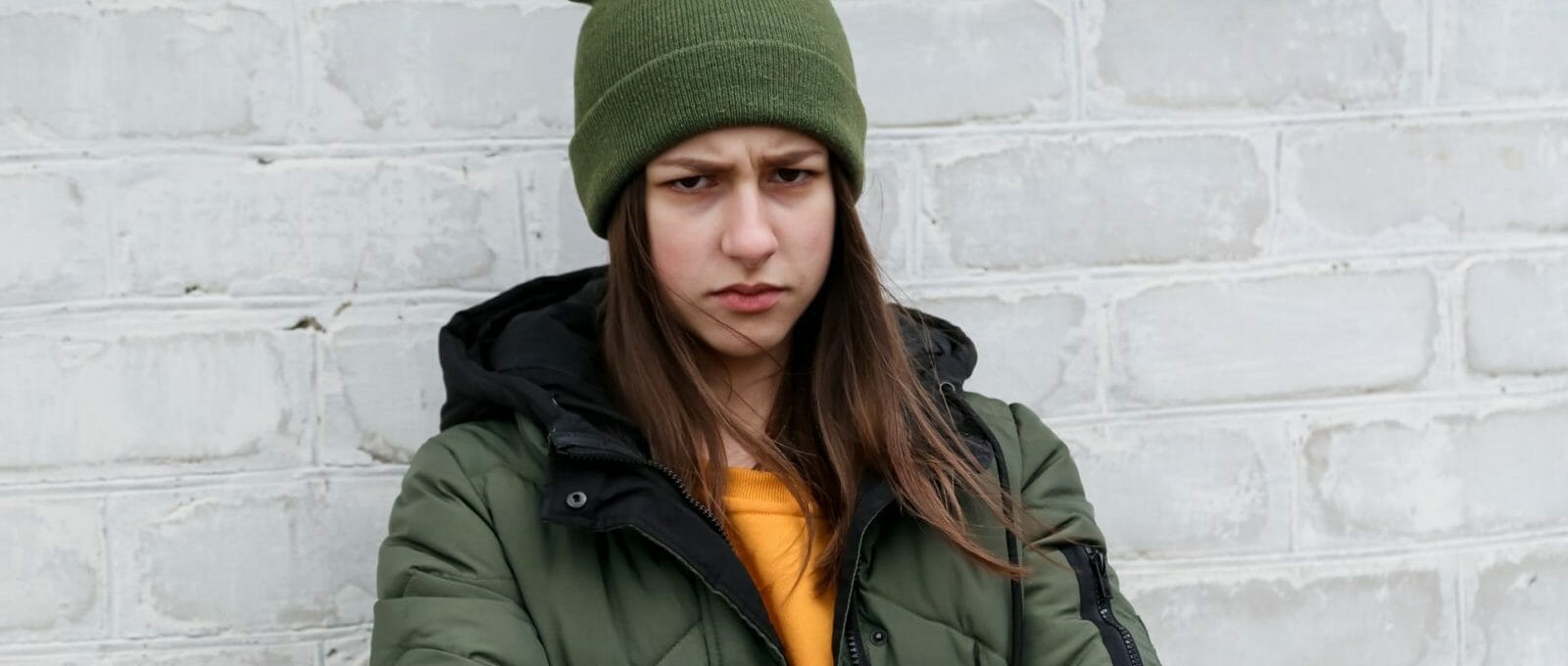 adolescente emburrada em frente a uma parede de tijolos brancos