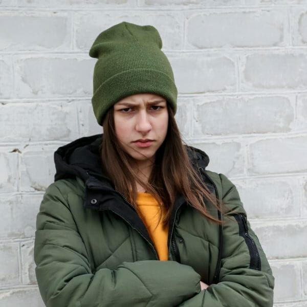 adolescente emburrada em frente a uma parede de tijolos brancos