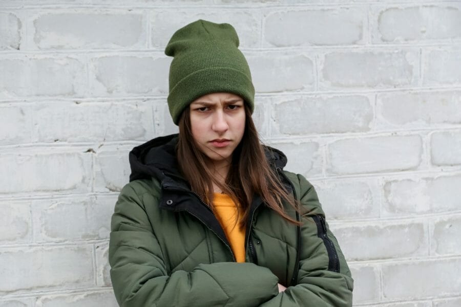 adolescente emburrada em frente a uma parede de tijolos brancos