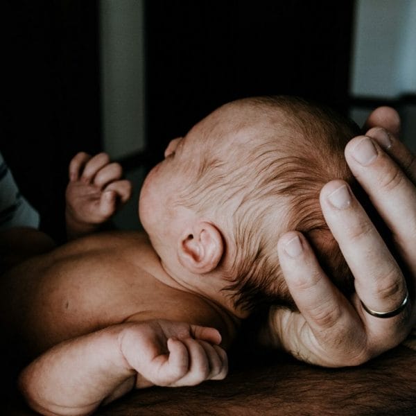 pai segurando bebê no colo com delicadeza, com ambas as mãos na parte de trás da cabeça