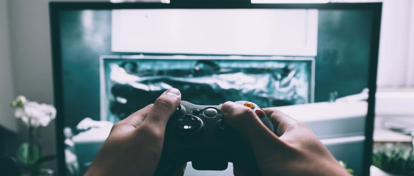 imagem de tela de computador e adolescente segurando controle de videogame em frente a ela