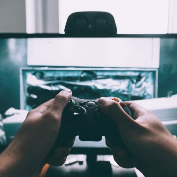 imagem de tela de computador e adolescente segurando controle de videogame em frente a ela