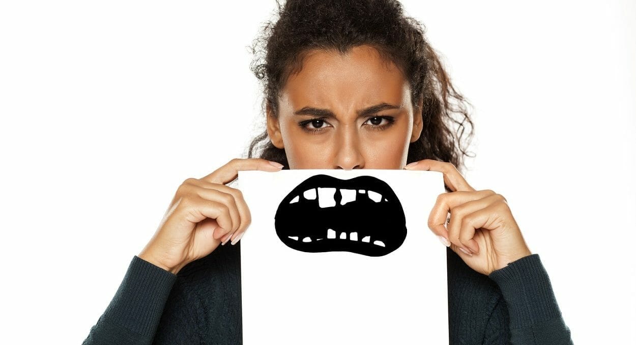 adolescente com um cartaz em frente ao rosto, escondendo o sorriso e mostrando dente escuro
