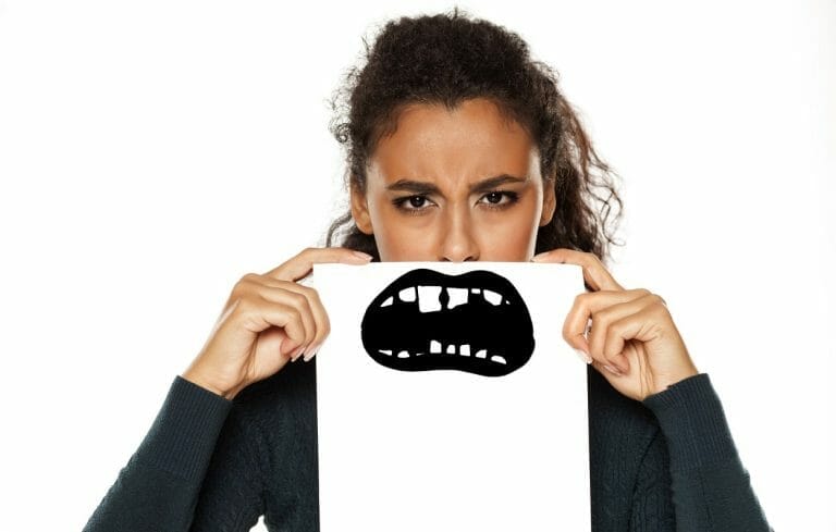 adolescente com um cartaz em frente ao rosto, escondendo o sorriso e mostrando dente escuro