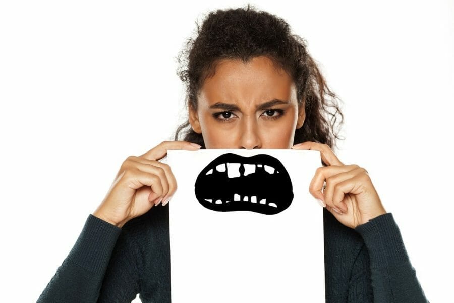 adolescente com um cartaz em frente ao rosto, escondendo o sorriso e mostrando dente escuro